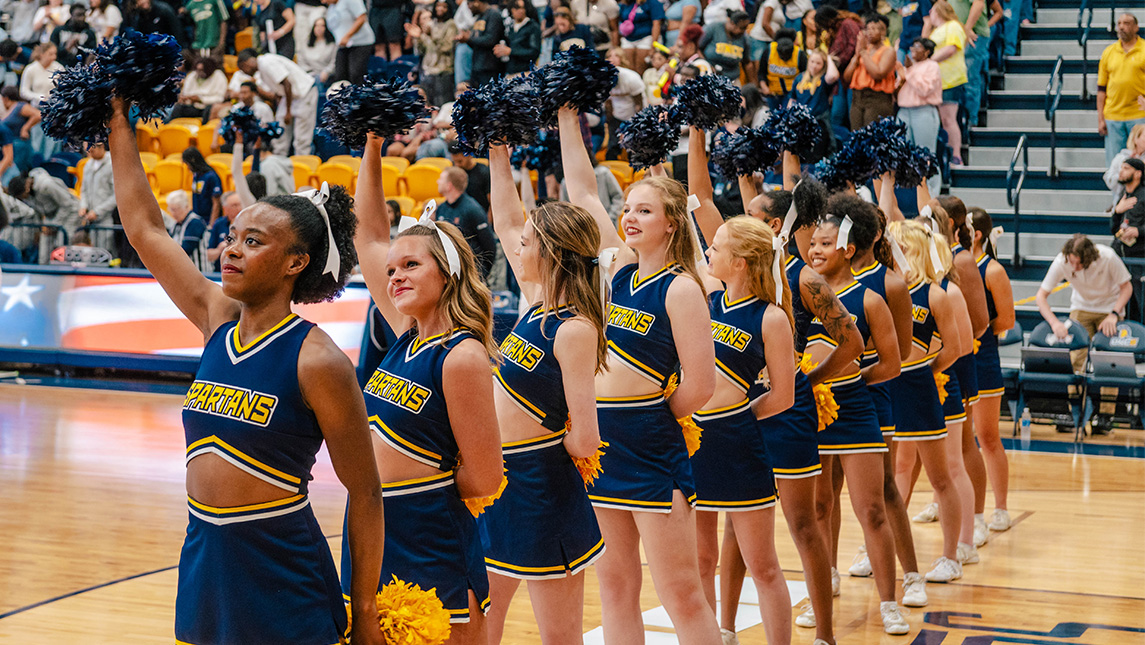 UNCG cheerleaders perform on a basketball court for a crowd.