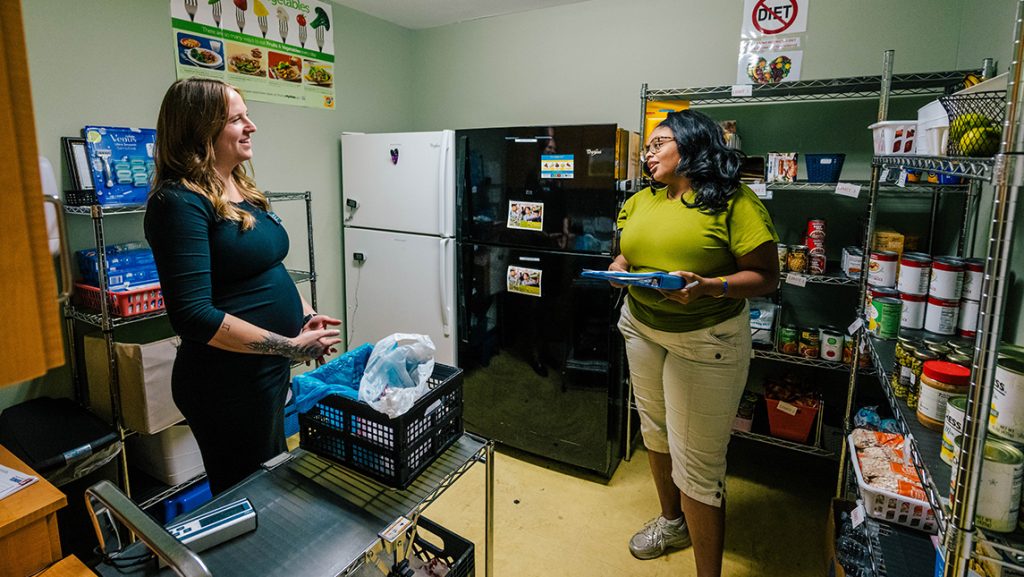 Two women check canned food on shelves.