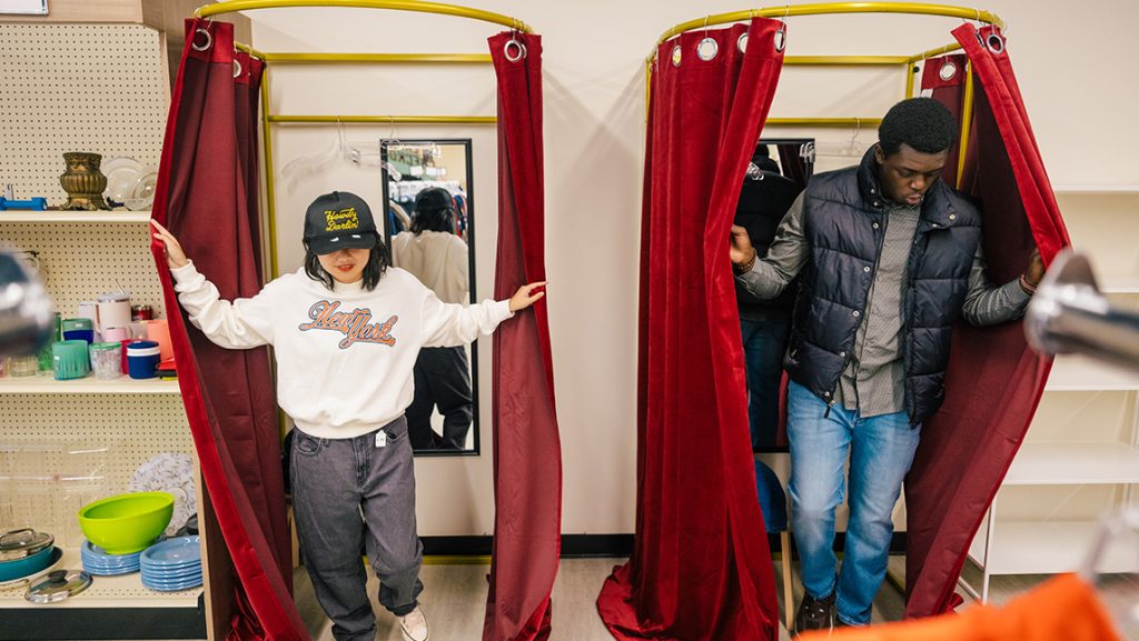 Two people throw back the curtains while stepping out of dressing rooms.