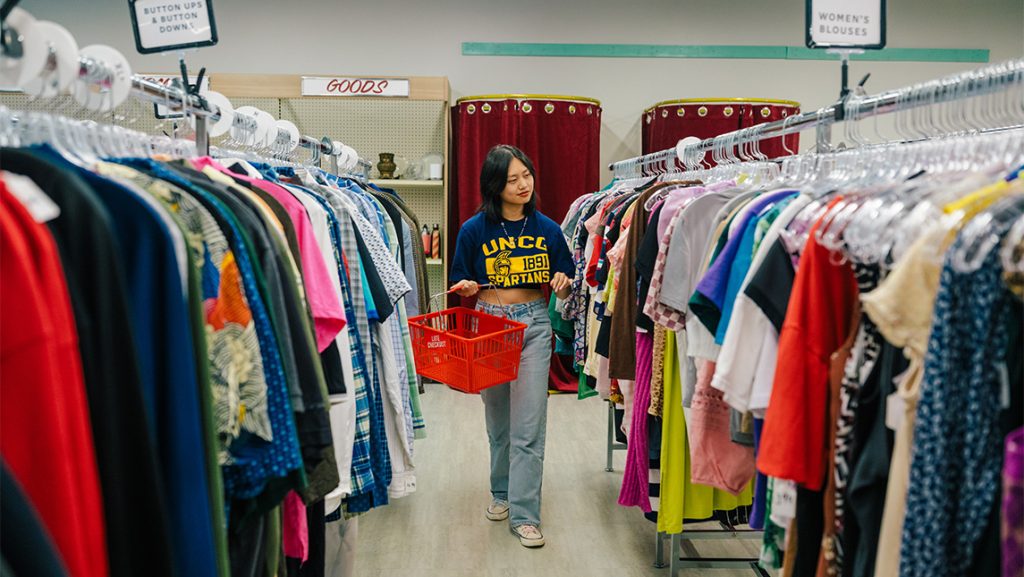 A woman walks between two racks of clothes.