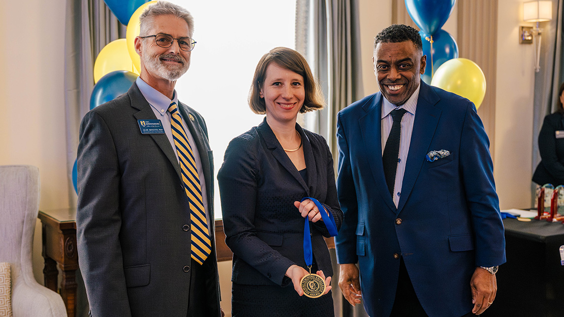 UNCG faculty Insa Lawler holds a medal alongside Chancellor Gilliam and Provost Boyette.