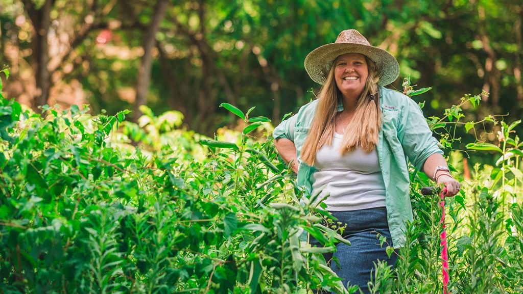 Sally Koerner wears a straw hat in a field of tall grass.