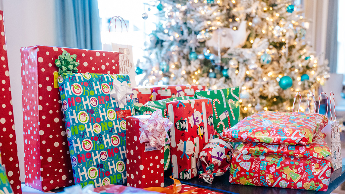 Gift-wrapped presents stacked in front of a Christmas tree.